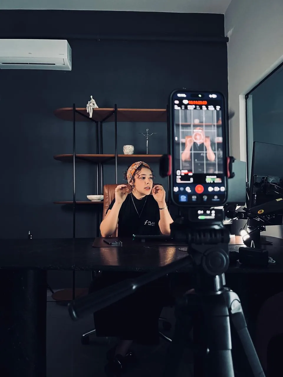 Maria Fernanda gravando conteúdo em estúdio, com celular em tripé e iluminação montada.